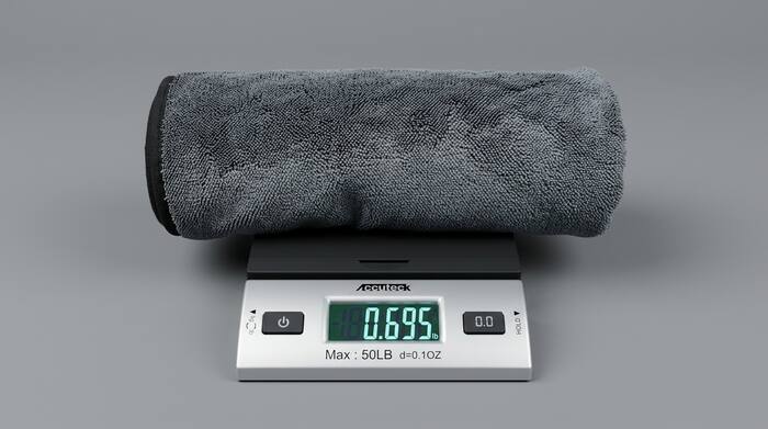 Competitor's gray microfiber towel rolled on an Accuteck digital postal scale — the display reads 0.695 lb (about 0.7 lb)